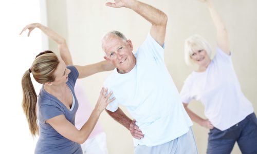 Portrait of an elderly man doing stretches and being assisted by a young instructor