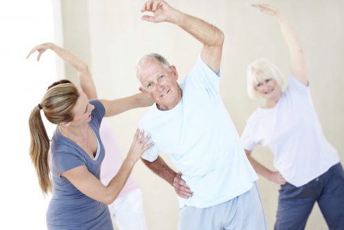 Portrait of an elderly man doing stretches and being assisted by a young instructor